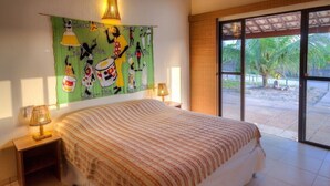 Une chambre avec un grand lit, une table de chevet avec une lampe, une tapisserie murale et une vue sur l’extérieur grâce à une porte-fenêtre coulissante.