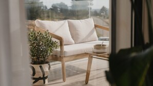 Ein Balkon mit einem Holzstuhl, einem weißen Sofa, einem kleinen Tisch mit einer Schale und einem Blumentopf.