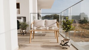 Ein moderner Balkon mit Holztisch und -stühlen, Blumentöpfen und Blick auf die umliegende Landschaft.