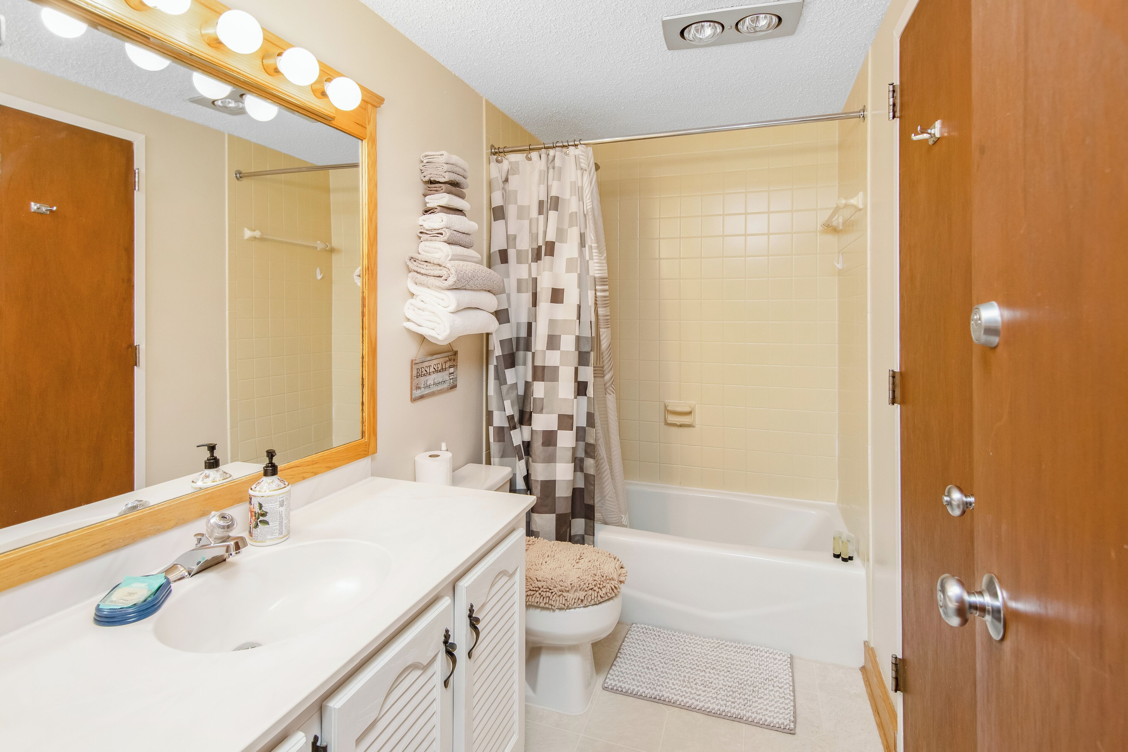 A bathroom with a white sink, a mirror with lights, a shower curtain, and a toilet.