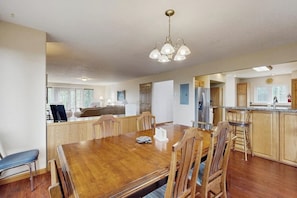 Un vaste espace dédié à la salle à manger, avec une table et des chaises en bois, une cuisine dotée de meubles en bois et un luminaire suspendu.