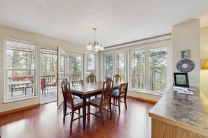 A dining room with a large table and chairs, large windows, and a view of trees. - Spacious and secluded home with mountain views, gas grill, decks & home office (Rapid City)