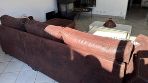 Ein Wohnzimmer mit einem braunen Ledersofa, einem Flachbildfernseher, einem kleinen Tisch mit einer Dekoration und einem schwarzen Herd.