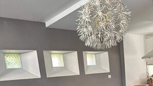 Ein moderner Essbereich mit einem langen Tisch und sechs blau gepolsterten Stühlen. Drei Fenster mit weißen Rahmen sind in der Wand eingelassen.