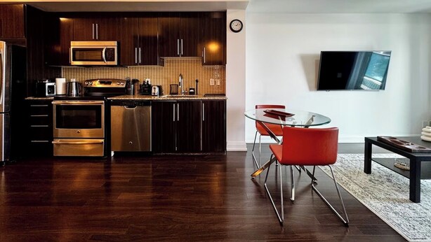 A modern kitchen with dark wood cabinets, stainless steel appliances, and a glass dining table with red chairs. - Modern Designed Home (Sebright)