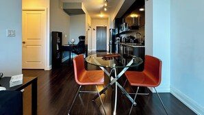 A modern kitchen with dark cabinets, a stainless steel refrigerator, and a glass dining table with two orange chairs. - Modern Designed Home (Sebright)