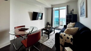 A modern living room with a glass dining table, red chairs, a dark sofa, and a TV mounted on the wall. - Modern Designed Home (Sebright)