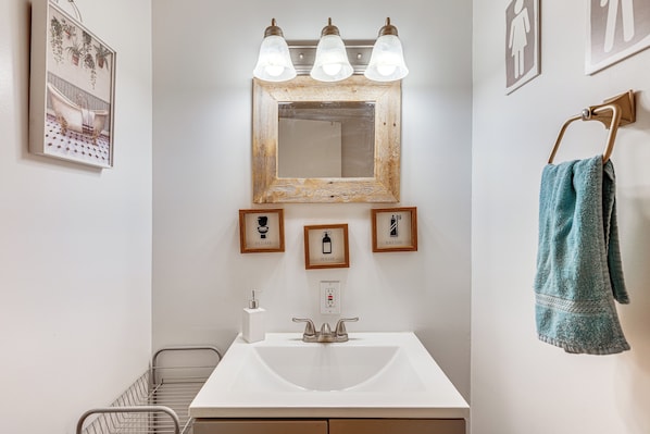 A bathroom with a white sink, a mirror with three lights, and framed pictures above the mirror. - Lake & Mtn Views: Vermont Couple's Retreat! (Barton)