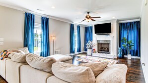 Ein Wohnzimmer mit beiger Couch, einem flachbildfernseher über einem Kamin und blauen Vorhängen.