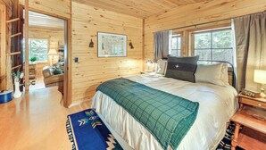 Een slaapkamer in een houten hut met een groot bed, een nachtkastje, een klok en een raam met gordijnen.