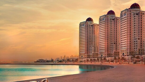 Un hotel frente a la playa con varios edificios de gran altura, una playa de arena y sillas de descanso.