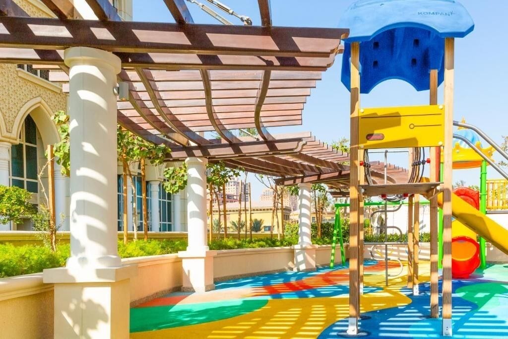 Un espace de jeux extérieur avec des marquages colorés au sol, une structure d’escalade et un pavillon ombragé.