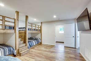 A room with bunk beds, wooden beams, a white door, and a television on the wall. - Baldwin Lakefront Home: Dock, Fire Pit & Trails! (Baldwin)