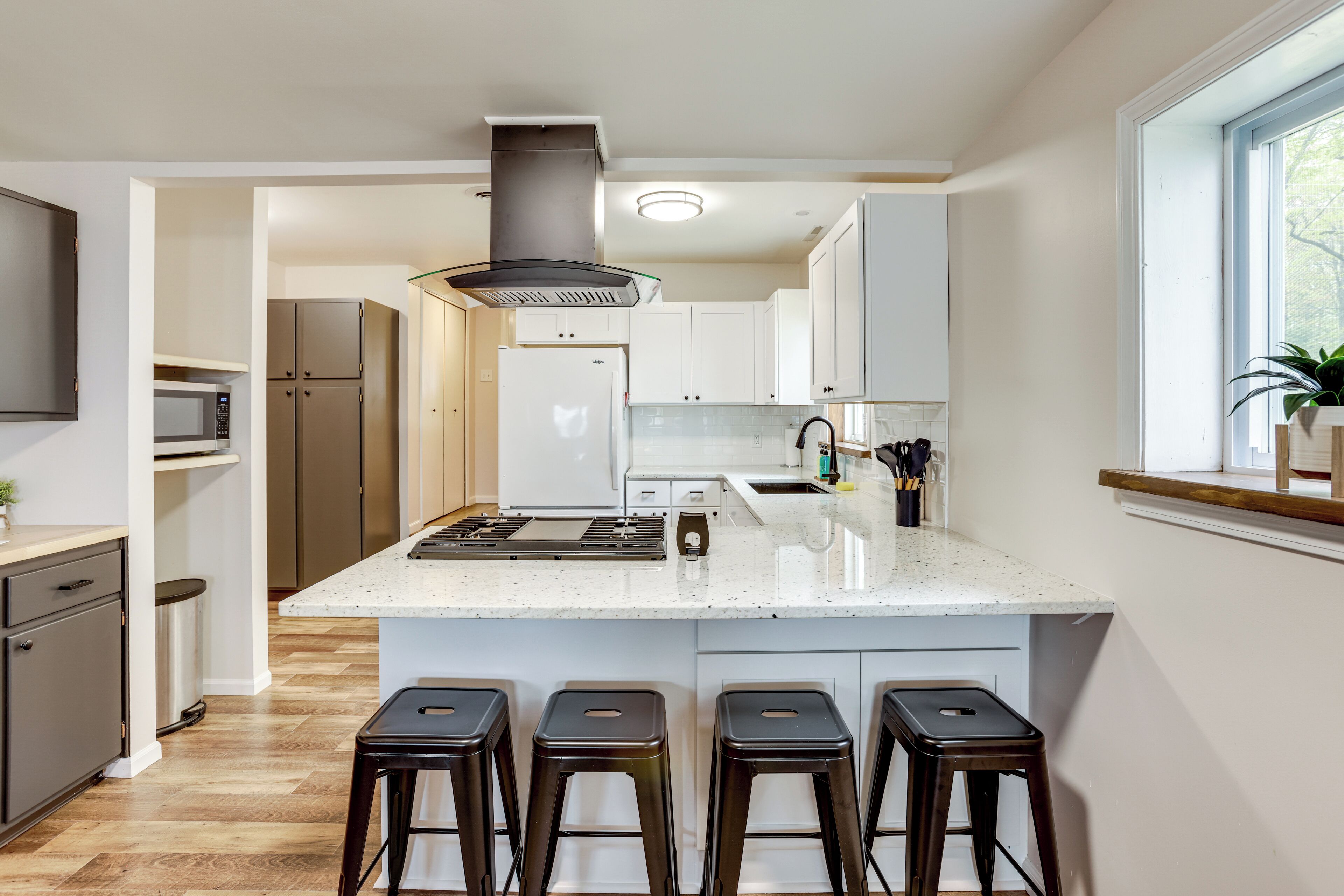 A modern kitchen with a central island, bar stools, stainless steel appliances, and a window with a view.