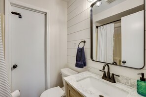 A bathroom with a white toilet, a sink with a marble countertop, a mirror, and a towel hanging on a towel ring. - Baldwin Lakefront Home: Dock, Fire Pit & Trails! (Baldwin)
