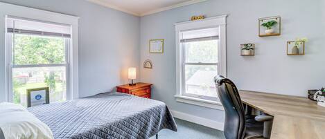 Un dormitorio con cama, escritorio y silla, una mesita de noche con lámpara, y tres cuadros en la pared.