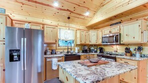 A kitchen with wooden cabinets, stainless steel appliances, granite countertops, and a sign that reads "The Mountains Are Calling". - 10 Mi to Main St Murphy: Cabin w/ Covered Deck! (Murphy)