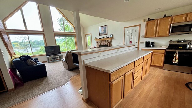 A modern kitchen with wooden cabinets, a large island, and a dining area with a sofa and TV. - Relax at Bear Hug House on Bear Lake Manawa Wi.– Private Pond & Easy Lake Access (Manawa)