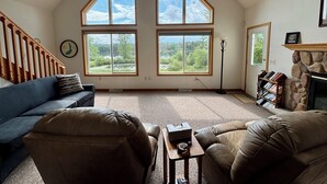A spacious living room with a high ceiling and large windows offering a view of a lake and trees. - Relax at Bear Hug House on Bear Lake Manawa Wi.– Private Pond & Easy Lake Access (Manawa)