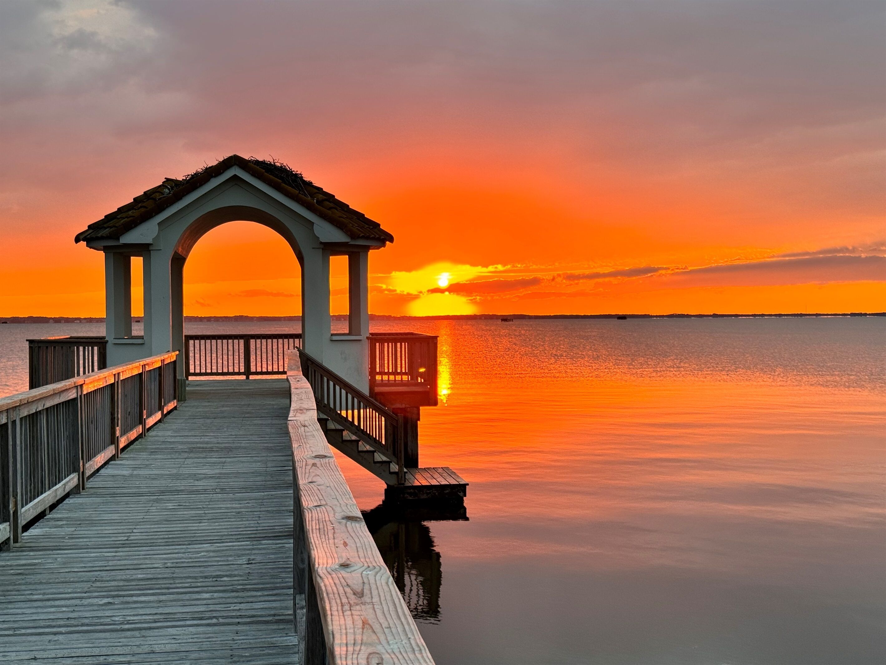 Eine Holzstege führt zu einem Pavillon mit Blick auf den Sonnenuntergang über dem Wasser.