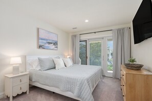 A bedroom with a bed, nightstand, and a view of the outdoors through a sliding door. - New,HotTub,PoolHeat,SoundSide,OceanViews,Gameroom (Corolla)