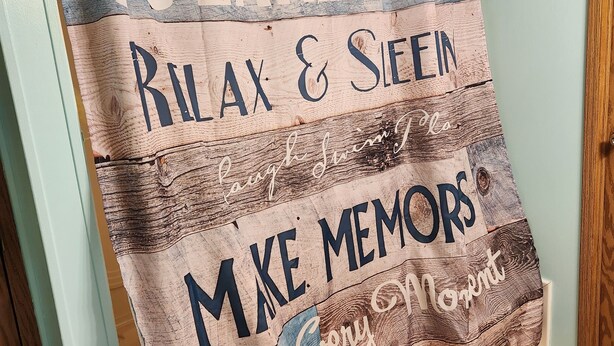 A wall hanging with the text "LAKE HUIZ RELAX & SLEEP MAKE MEMORIES Every Moment Enjoy".