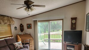 A living room with a sofa, a TV stand, a ceiling fan, and a sliding glass door leading to an outdoor area.