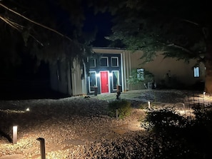 A building with a red door, surrounded by gravel and trees, at night.
