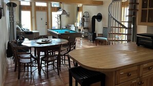 Amplia sala de estar con mesa de billar, mesa de comedor y zona de cocina con escalera en espiral.