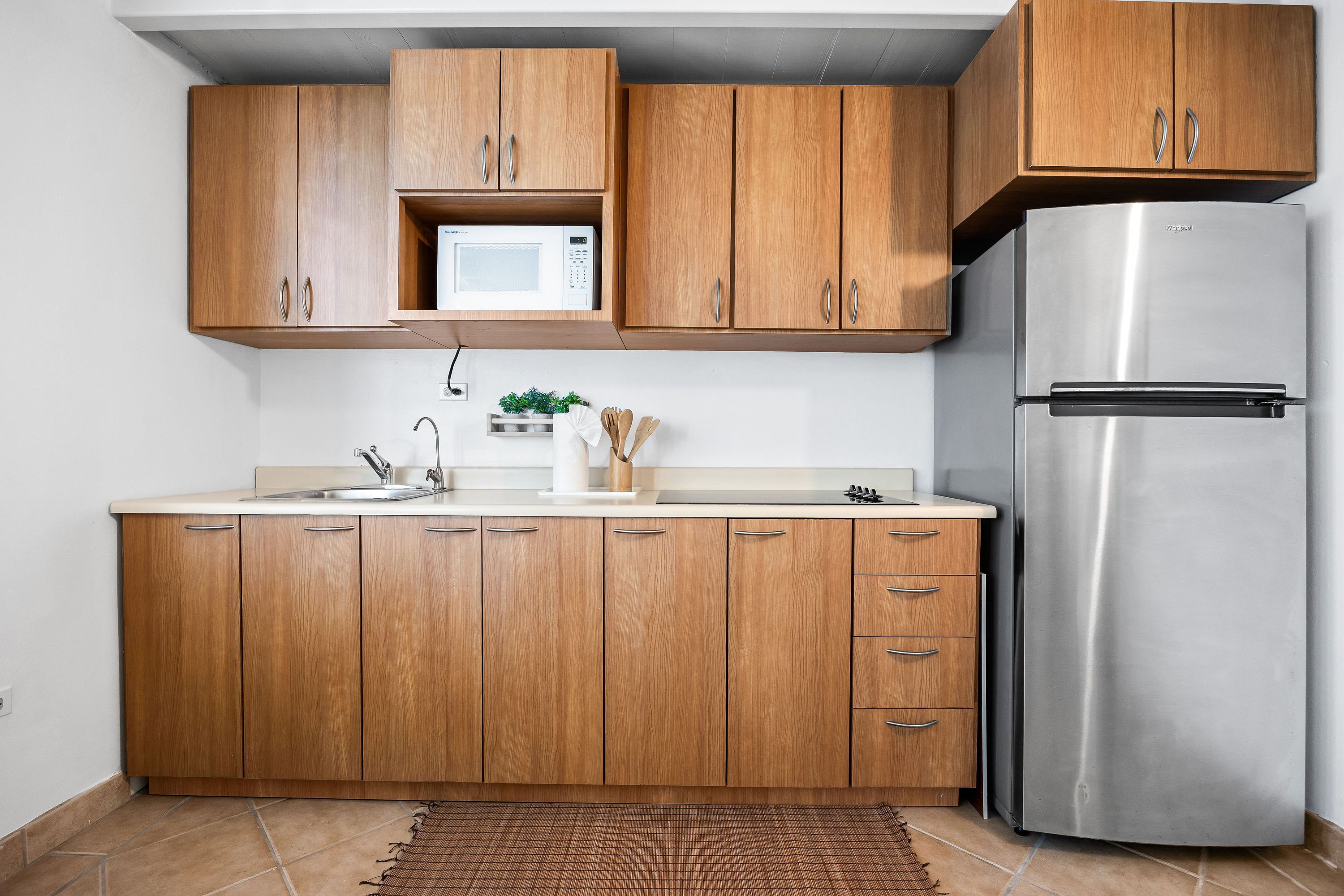 Eine moderne Küche mit Holzschränken, einem Edelstahlkühlschrank und einer Mikrowelle.