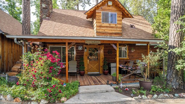 A log cabin with a porch, a sign reading "Witch of the Lake," and a small garden with pink flowers.