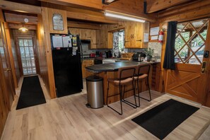 A kitchen with wooden cabinets, a black refrigerator, a stainless steel trash can, and a bar area with stools.