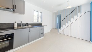 Een moderne keuken met grijze kastjes, een zwart aanrecht en een ingebouwde oven. Er is een trap met blauwe leuningen die naar een ander niveau leidt.