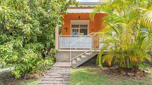 A house with a stone staircase leading to a white porch, surrounded by lush greenery and a palm tree. - ALAMANDA (1 to 3 people) (DESHAIES)