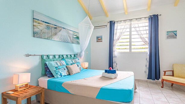 A bedroom with a bed, bedside tables, a nightstand, a window with curtains, and a painting on the wall. - ALAMANDA (1 to 3 people) (DESHAIES)