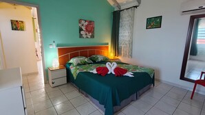 A hotel room with a bed, a nightstand, a lamp, a window with curtains, and a door. - PAPYRUS (1 to 3 people) (DESHAIES)