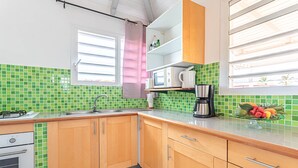 A kitchen with green-tiled backsplash, wooden cabinets, a microwave, and a fruit bowl on the counter. - PAPYRUS (1 to 3 people) (DESHAIES)