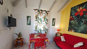 A living room with a red sofa, a dining table with chairs, a TV mounted on the wall, and tropical-themed artwork. - PAPYRUS (1 to 3 people) (DESHAIES)