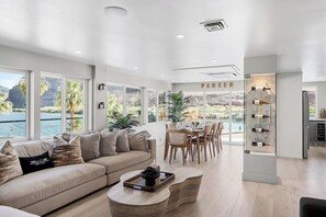 A spacious living area with a large window overlooking a body of water, a dining area with a view, and a wine display. - Waterfront Private Dock, Boat Ramp & River VIEWS! (Parker)