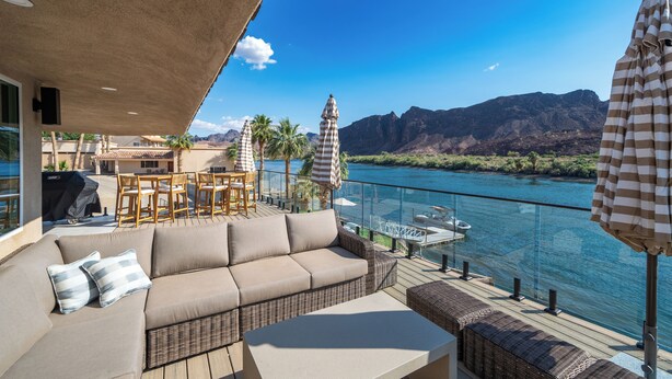 Ein Balkon mit einer Couch, Stühlen und einem Tisch mit Blick auf einen Fluss und dahinter Berge.