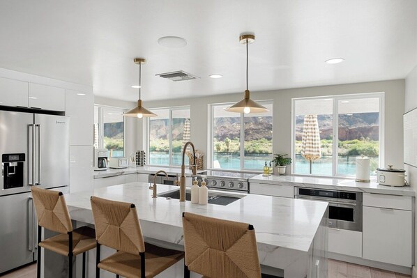 A modern kitchen with a large island, stainless steel appliances, and a view of a natural landscape. - Waterfront Private Dock, Boat Ramp & River VIEWS! (Parker)