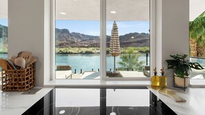 Eine Küche mit großem Fenster, das einen Pool und Berge blickt. Auf der Arbeitsfläche steht ein Korbwicker-Korb mit Küchenutensilien, ein Schneidebrett und zwei Flaschen.