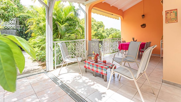 A covered outdoor patio with a table and chairs, surrounded by a white railing and lush greenery. - BALISIER (2 to 4 people) (DESHAIES)