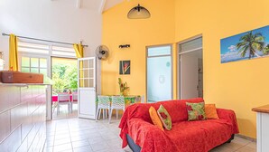 A bright living room with a red sofa, a dining area with a table and chairs, and a view of greenery outside. - BALISIER (2 to 4 people) (DESHAIES)