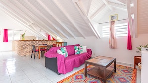 Een ruime loft met hoge plafonds, een gezellige zithoek met een bank en een salontafel, een keuken met een bakstenen muur en een kleurrijk vloerkleed.