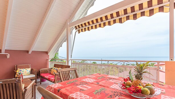 Een overdekt terras met een eettafel, stoelen en uitzicht op de oceaan.