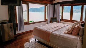 A bedroom with a bed, a television, and a view of a lake. - Casa Praia das Cigarras (Sao Sebastiao)