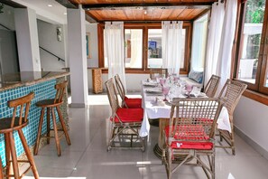 Comedor con sillas de mimbre y una mesa dispuesta para cuatro, con cojín rojo y mantel blanco.