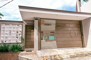 Una casa moderna con un portón marrón grande, un ventanal blanco decorativo y un camino de piedra que lleva a la entrada.