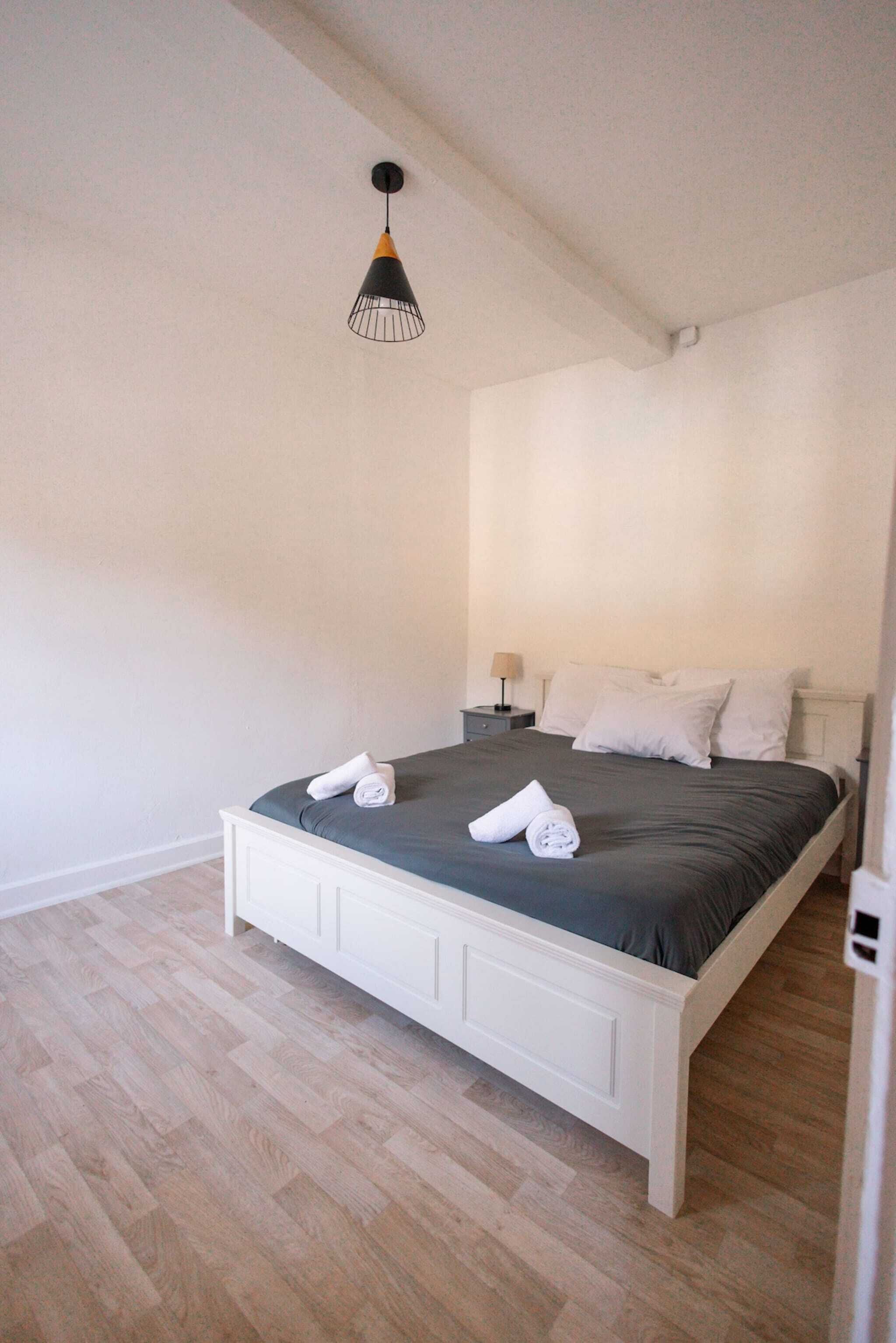 A bedroom with a white bed, a nightstand, a lamp, and a hanging light fixture.